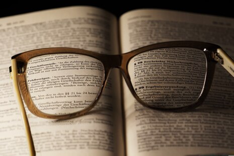Das Bild steht stellvertrend für die Aufgaben innerhalb der Abteilung II des Landesamtes für Steuern und Finanzen. Darauf abgebildet ist ein Gesetzesbuch, welches aufgeschlagen ist. Auf der aufgeschlagenen Seite liegt eine Brille. Das Bild steht für den D